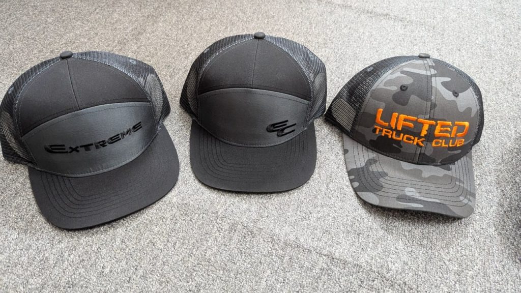 Three custom Richardson trucker hats โ black Extreme logo hat, black EC logo hat, and camo Lifted Truck Club hat, manufactured by Alvieva Apparel for Minnesota brands.